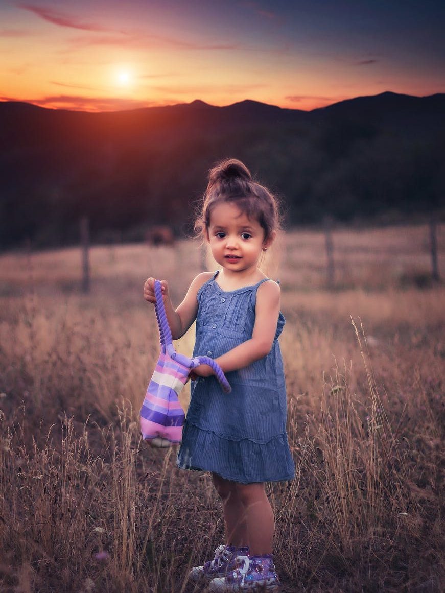 girl in blue dress standing on grass field during sunset
